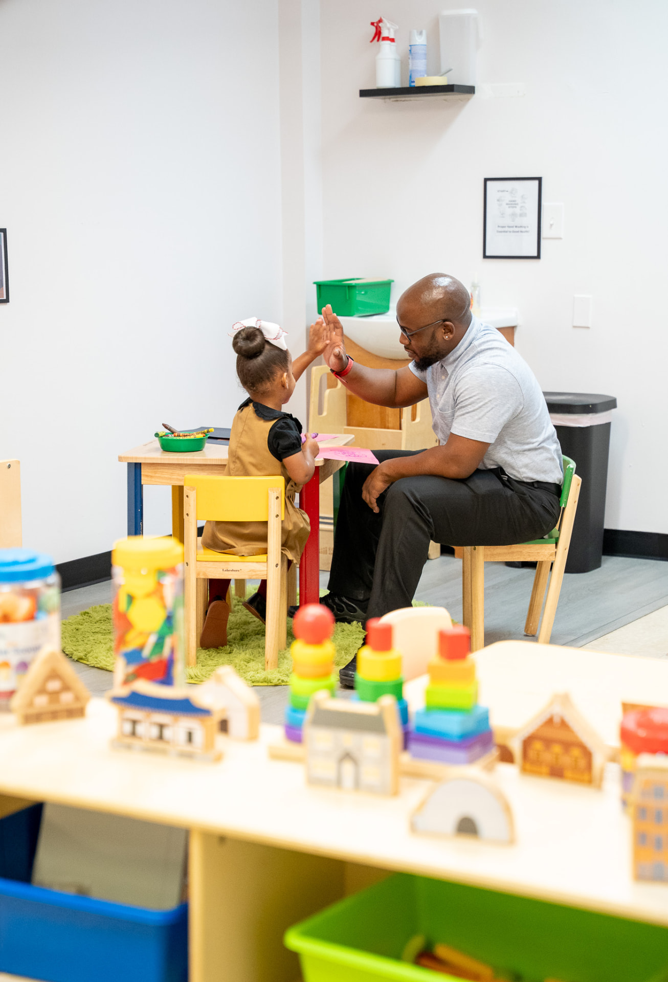 A teacher high-fiving a young student in a classroom at The Early Learning Institute